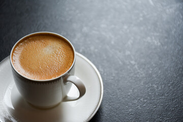 Morning hot espresso coffee or Americano in a white glass cup on a black background 2024. Beautiful white cup of black coffee on the black table.