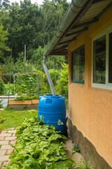 Water collection tank under a roof with a drain near a rural house.