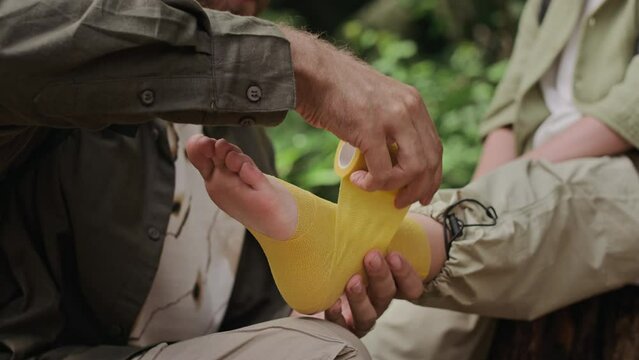 Father strapping his sons sprained ankle with tape while providing first aid outdoors in forest