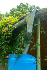 Water collection tank under a roof with a drain in garden. Rain water harvesting architecture.
