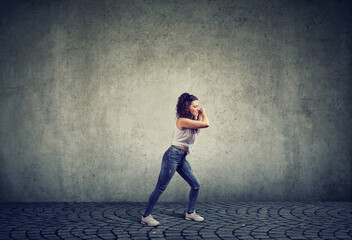 young woman pulling rope isolated on gray wall background 