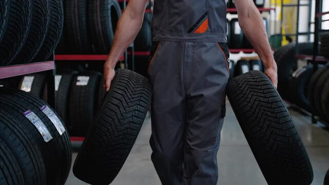 Male seller walking with new car tires in auto parts store