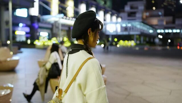 Slow-motion video of a young and cute Taiwanese woman in her 20s walking and spending time amidst beautiful illuminations at night in a high-end shopping mall area of Xinyi District, Taipei, Taiwan