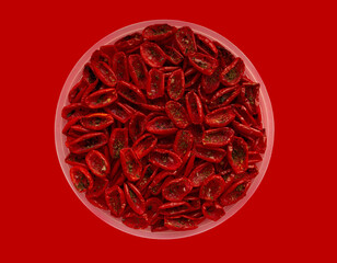 Tomatoes, dried in small pieces, lie in a plate on a red background.