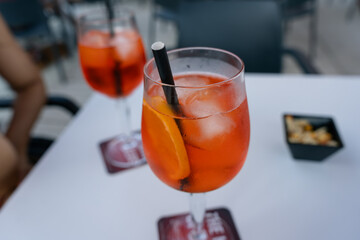 Glass of spritz cocktail standing on table with snacks in background. Glass of spritz cocktail is...