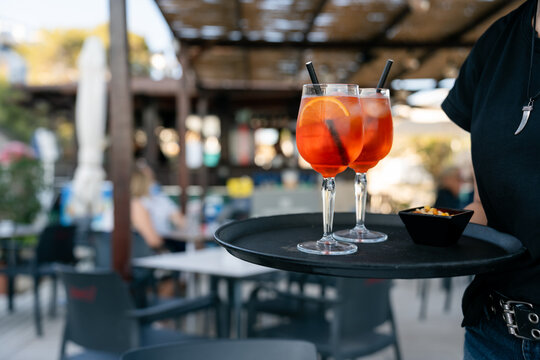Waiter holding tray with two spritz cocktails and snacks. Waiter is carrying a tray with two spritz cocktails and a bowl of snacks in a busy outdoor restaurant