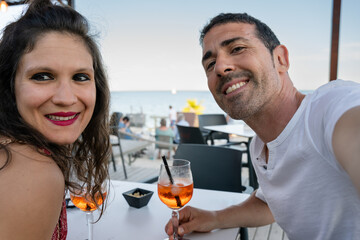 Couple taking selfie while enjoying drinks at beachfront restaurant. Couple is enjoying a romantic moment, taking a selfie while sipping cocktails at a beachfront restaurant
