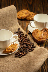 Coffee cups, cookies and coffee beans on the wooden background.