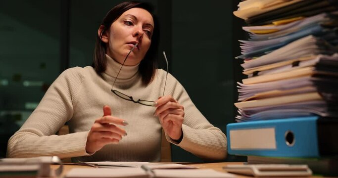 Exhausted businesswoman looks at stack of folders and papers
