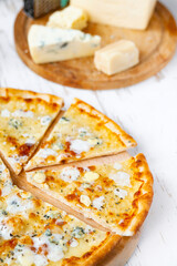 Pizza quattro formaggi on a wooden board .four cheese pizza and fresh ingredients for a four cheeses Italian pizza on a white wooden desk .