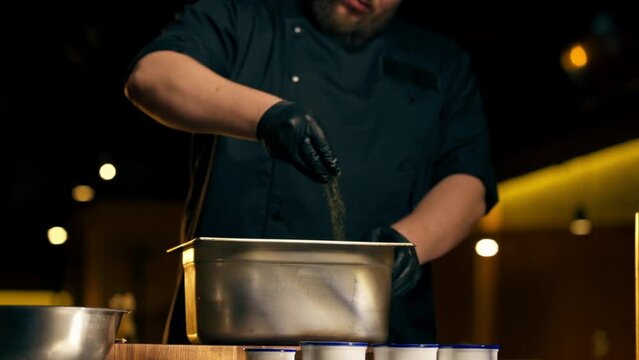 vertical video in a restaurant in a rib bar in the central hall a chef in black gloves sprinkles raw pork meat in an iron container with various spices