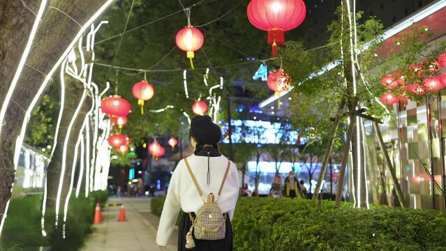 Slow-motion video of a young and cute Taiwanese woman in her 20s walking and spending time amidst beautiful illuminations at night in a high-end shopping mall area of Xinyi District, Taipei, Taiwan