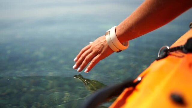 A person is touching the water with their hand. The water is clear and calm. The person is wearing a yellow life jacket.
