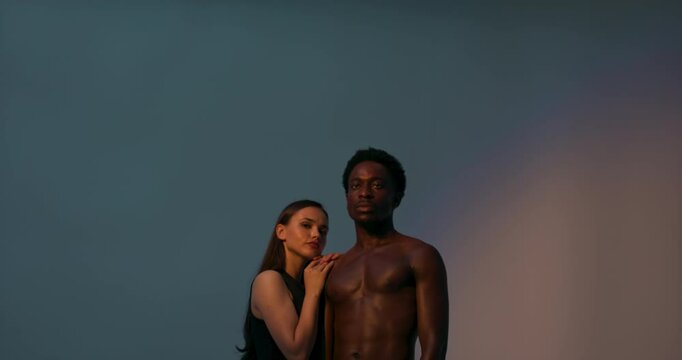Beautiful multinational couple american dark skinned man and white woman in studio with bright light isolated posing showing fit body strengths. Abstract multi coloring concept.