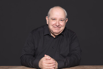 Portrait of a sexagenarian man with white hair and black shirt posing smiling looking at camera....