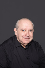 Portrait of a 60 years old man with white hair and blue eyes wearing a black shirt on a gray background with a calm attitude. Copy Space. Concept of aging