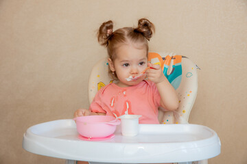 A little girl is sitting on a high chair eating at home