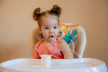 A little girl is sitting on a high chair eating at home
