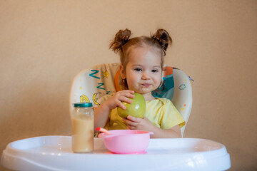 little girl is sitting on a high chair and eating a green apple	
