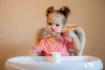 A little girl is sitting on a high chair eating at home