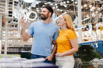 Smiling loving couple standing in decor department checking price on the lamp in the store