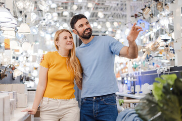 Smiling man pointing to the lamp, hugging woman, standing in the in decor department