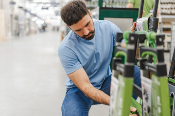 Young man shopping in construction supermarket choosing ladder