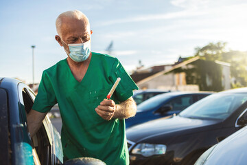 A mature male healthcare professional explains the testing procedure to a patient at a drive through testing site. The healthcare professional is holding a medical test kit.