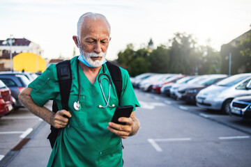 Shot of a mature male nurse standing in a parking lot in his scrubs, while typing on his smartphone...