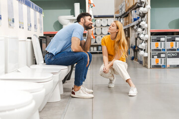 Fototapeta premium Young married couple choosing new toilet in hardware store