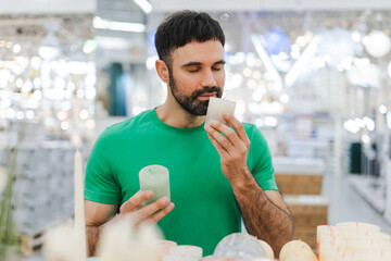 Young man closing eyes smelling a decorative candle in a store in the decor department