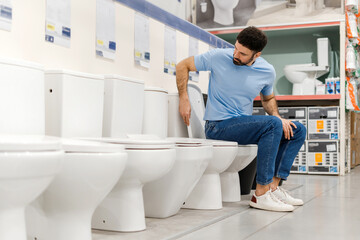 Young man sitting and choosing new toilet in hardware store, checking the quality