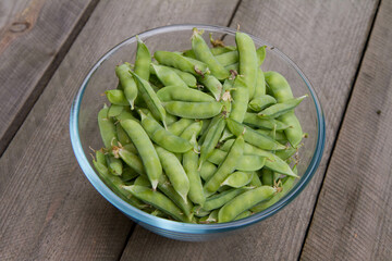 Freshly gathered pea pods in a bowl on a wooden table