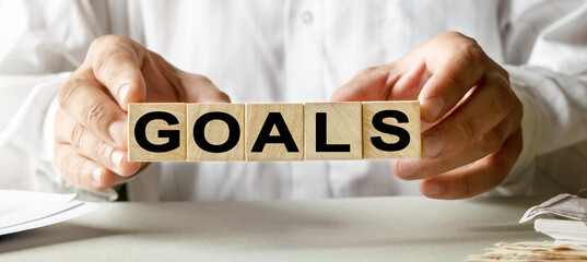 GOALS inscription on the texture of wooden cubes. A business man holds a cube in his hand. An inscription on a financial, business or economic theme.