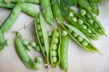 Freshly gathered pea pods , some open with seeds visible, on a wooden tray