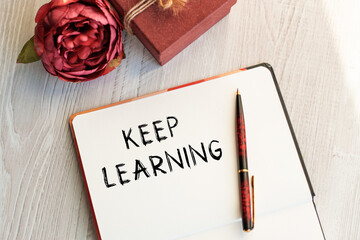 Notebook with inscription KEEP LEARNING on a light table along with a flower and a vintage gift box. Natural light. View from above. Festive concept.