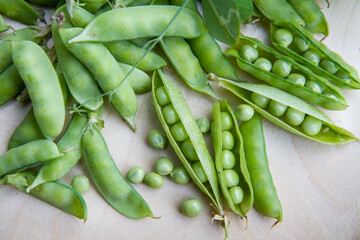 Freshly gathered pea pods , some open with seeds visible, on a wooden tray