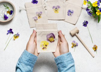 View from above of a small handmade fabric bag with hammered pansy flower prints. Step by step of creating a cloth bag with flower prints. Natural material craft for kids concept.