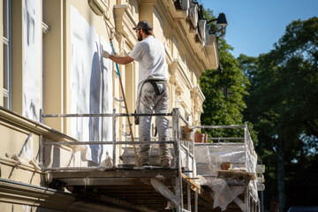 Worker painting and restoring the exterior of a historic building on scaffolding.