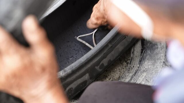 Car mechanic repairs punctured tire hit by nail on rim in service workshop. Close-up of a mechanic at a tire service shop changing a tire.