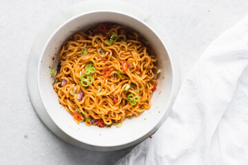 Overhead view of Spicy instant noodles with slices of green and red chili, spicy ramen noodles in a white ceramic bowl