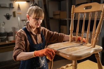 female craftsman in apron and shirt takes measurements with tape measure in her workshop. concept repair and restoration of old furniture.