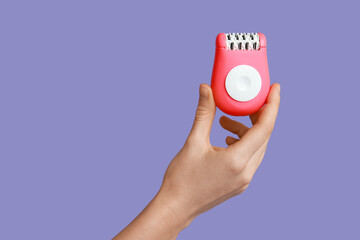 Female hand with modern epilator on purple background