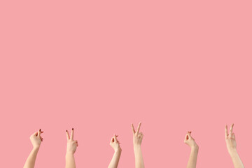 Female hands showing peace gestures and holding something on pink background