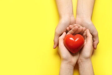 Hands of woman and child with red heart on yellow background