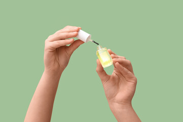 Female hands with bottle of cuticle oil on green background