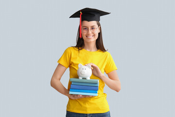 Young female graduate with books and piggy bank on grey background. Tuition fees concept