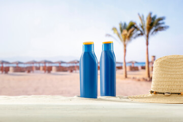 Blue containers for sun tan lotion and sunscreen oils on a bright table with tropical  beach and a sea and clear sky background.