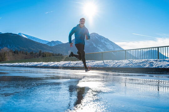 Man running on wet road in winter at sunny day