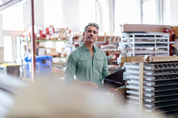 Mature businessman holding file folder and examining inventory in factory